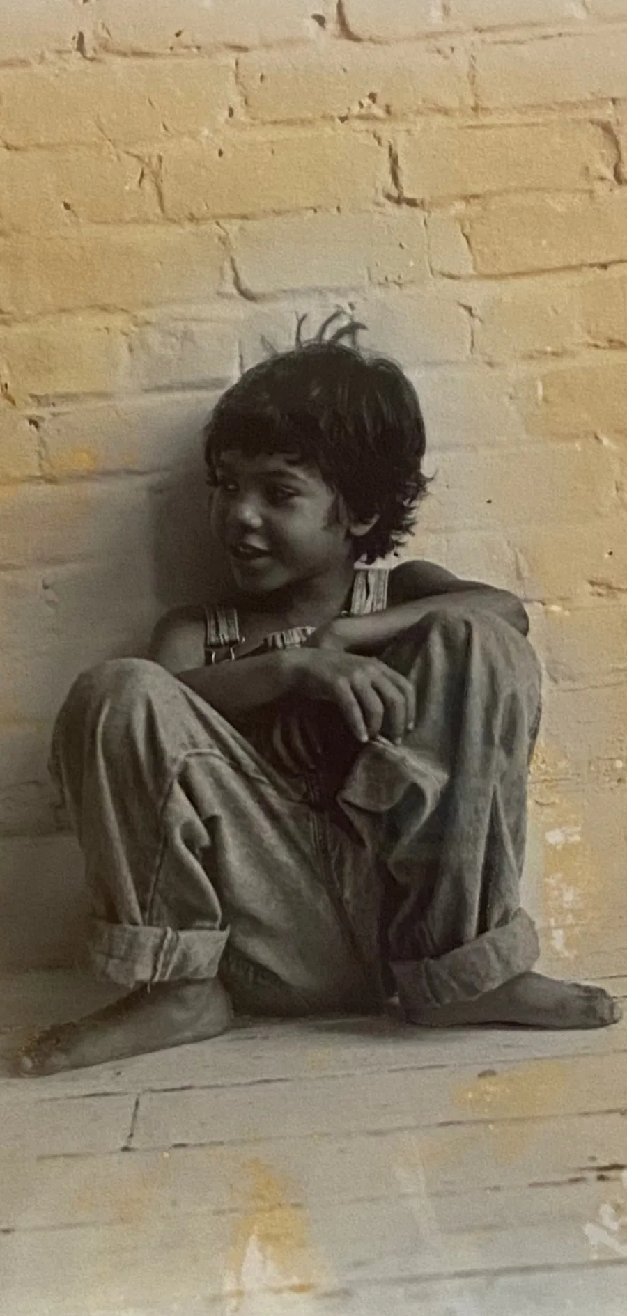 Mathieu as a child in New Orleans, seated barefoot against a painted brick wall