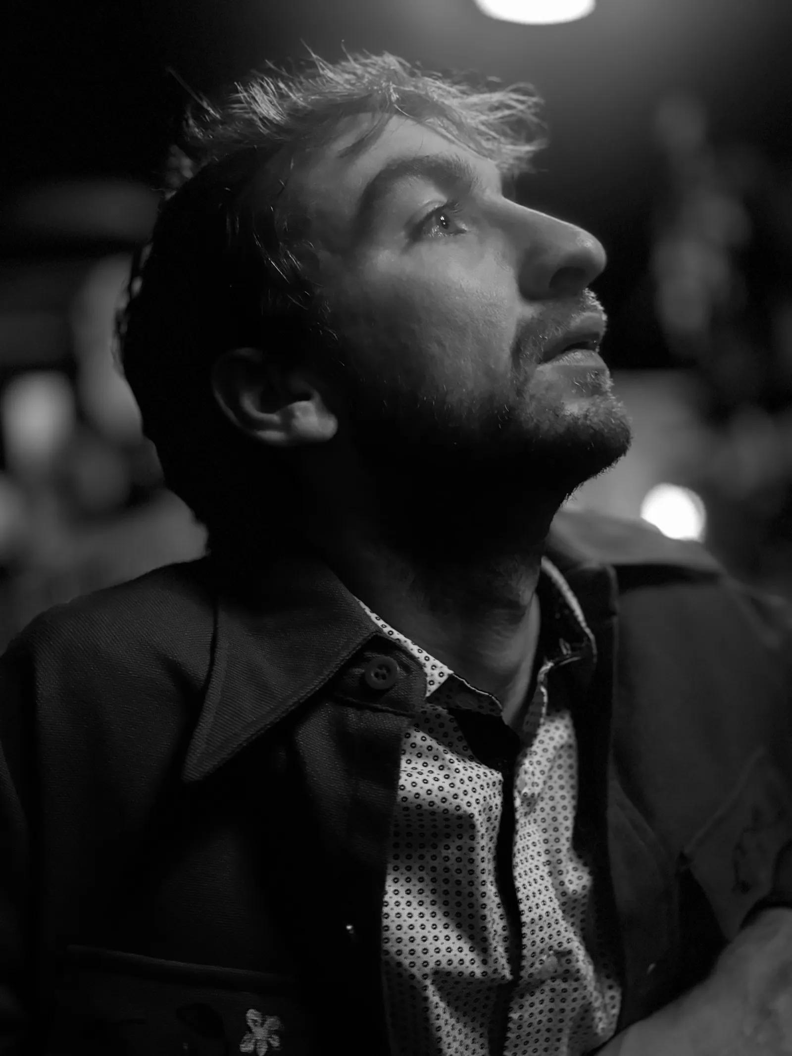 Untitled (The Light), black and white photograph by Mathieu: a man looking up into the light of a music room