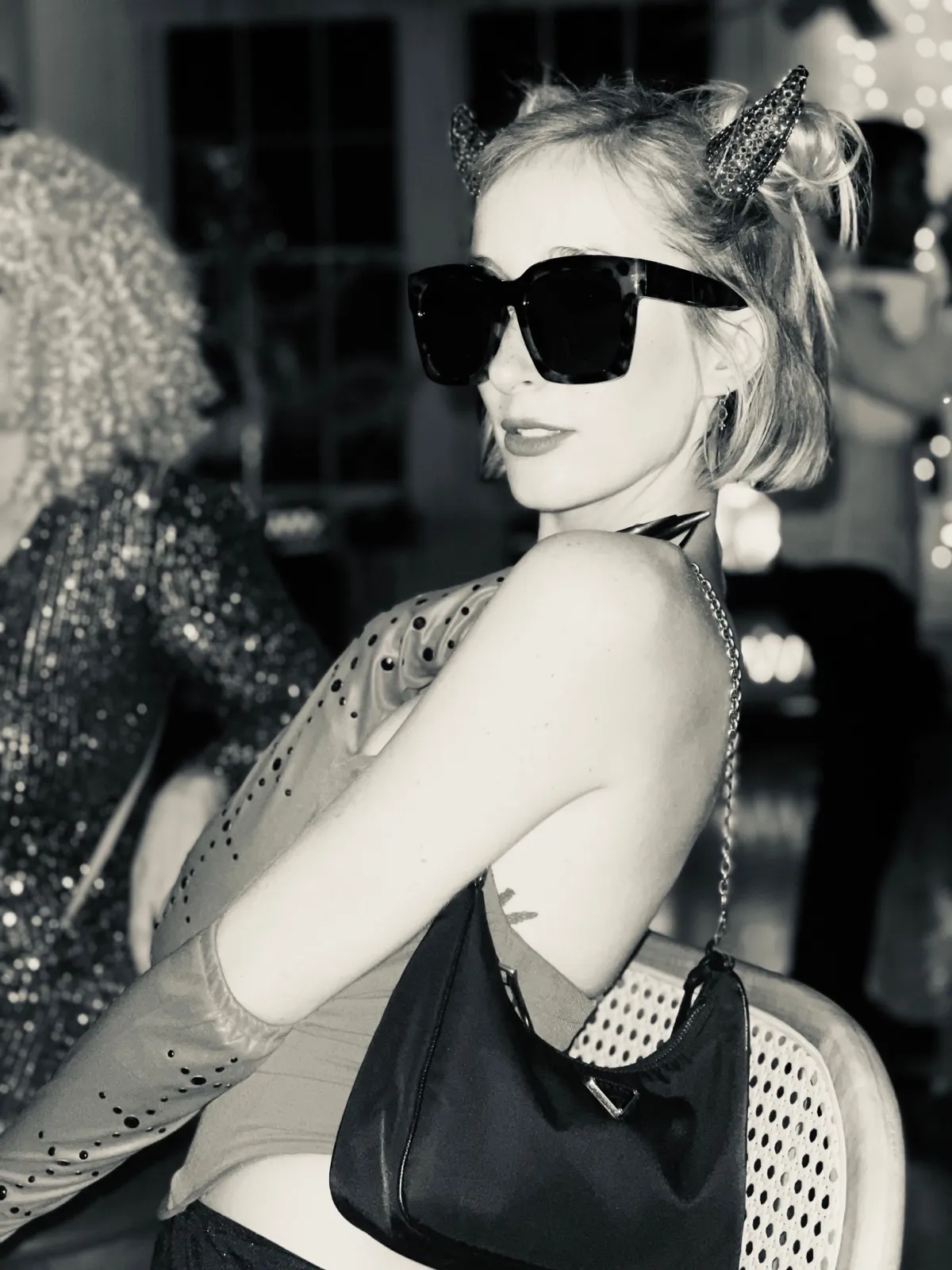 Untitled (Horns), black and white photograph by Mathieu: a woman in oversized sunglasses and costume horns glancing back at a party