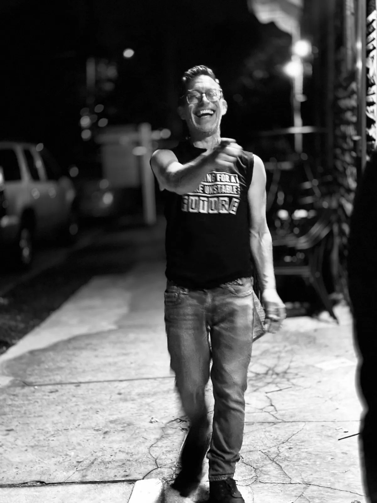 Untitled (The Laugh), black and white photograph by Mathieu: a man laughing on a night sidewalk, pointing at the camera