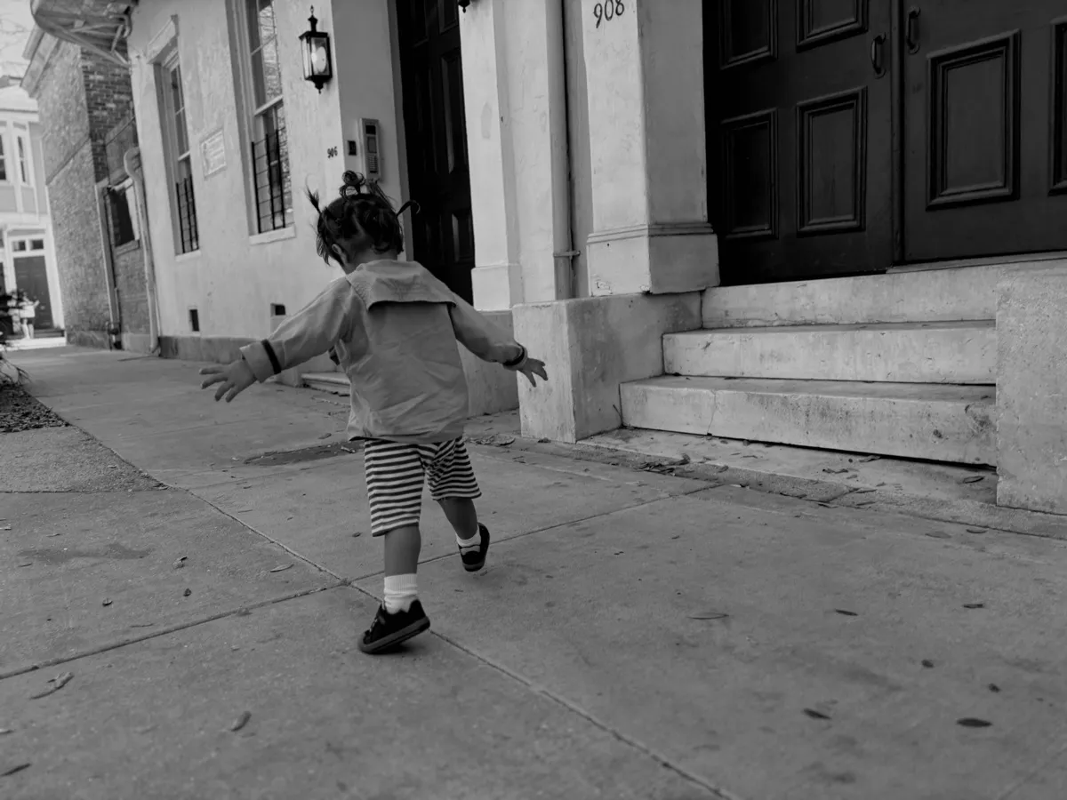 Untitled (Running), black and white photograph by Mathieu: a small child running down a French Quarter sidewalk, arms out