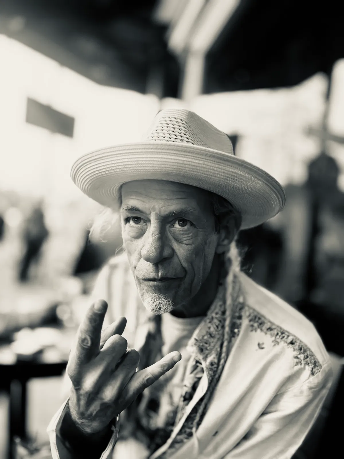 Untitled (Straw Hat), black and white photograph by Mathieu: a man in a straw hat holding two fingers up toward the camera