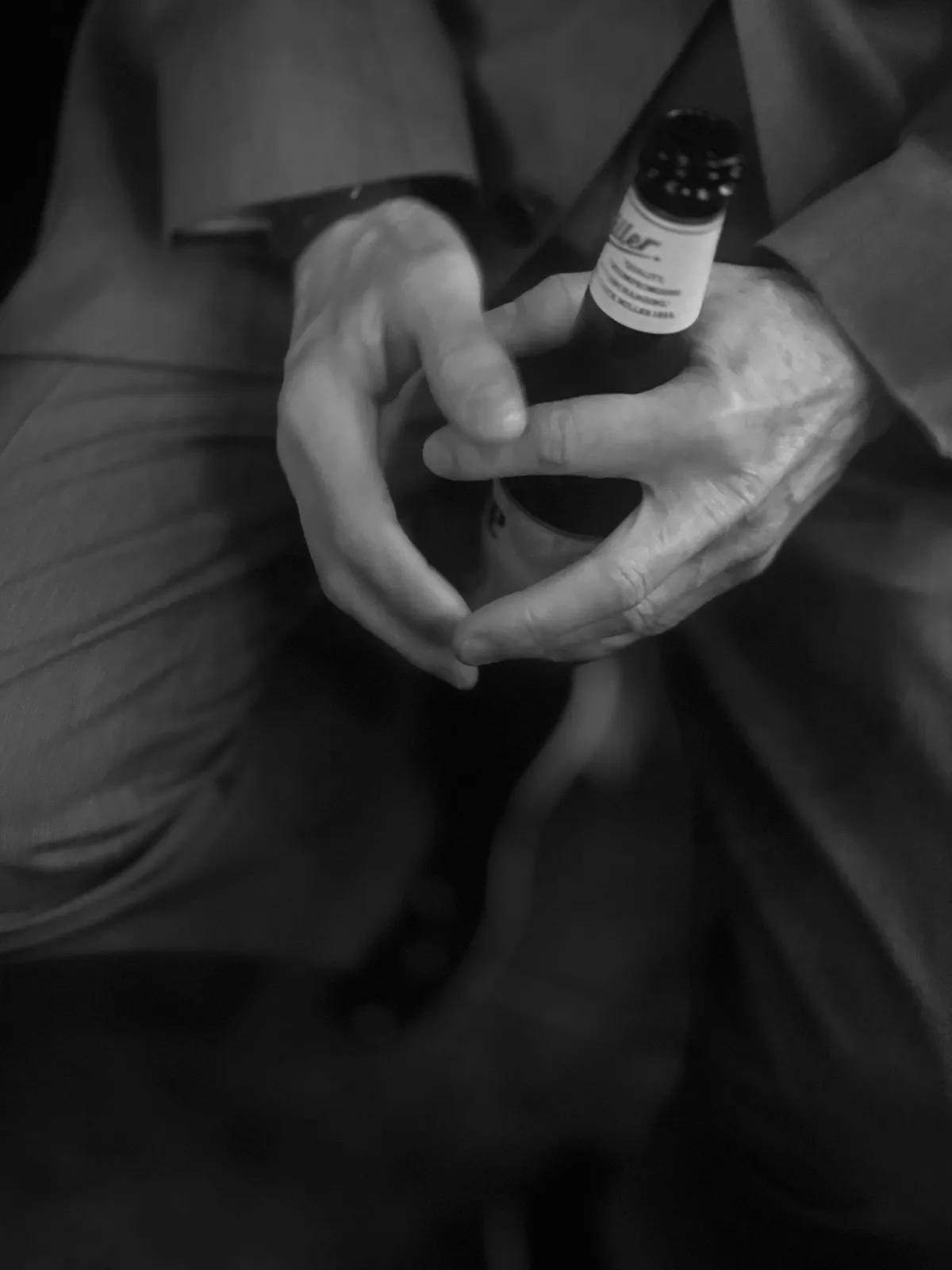 Untitled (The Bottle), black and white photograph by Mathieu: weathered hands cradling a beer bottle